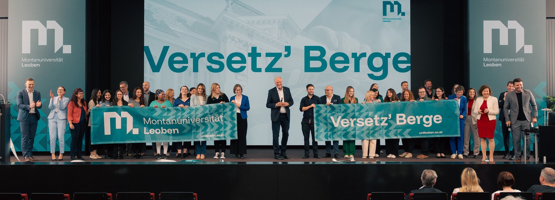 Gruppenfoto mit Mitarbeiterinnenen und Mitarbeitern der Montanuni auf der Bühne mit dem Motto Versetz' Berge.